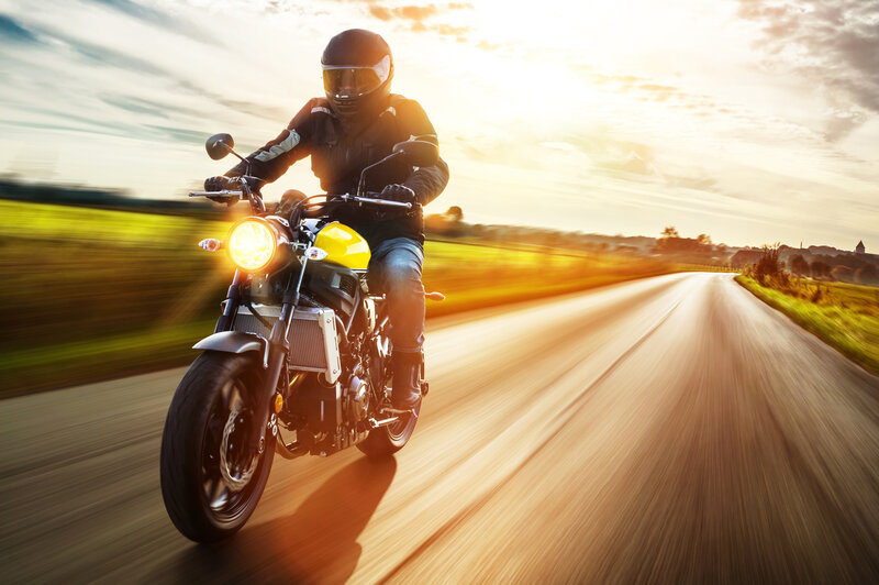 Motorradfahrer auf einer offenen Landstraße bei Sonnenuntergang, mit kompletter Schutzausrüstung und Helm. | © Fotolia_124935953