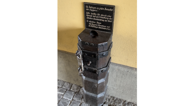 Historischer Spendenkasten in der Fuggerei in Augsburg mit Hinweistafel zur Unterstützung der Sozialsiedlung  | © Ringhotels e.V., Foto: SK