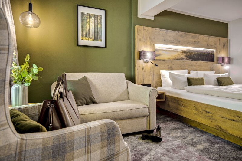 Stilvolles Doppelzimmer mit waldgrüner Wand, gemütlichem Sofa und großem Doppelbett im Ringhotel Sonnenhof in Baiersbronn, einem 4-Sterne-Hotel im Schwarzwald. | © Ringhotel Sonnenhof in Baiersbronn