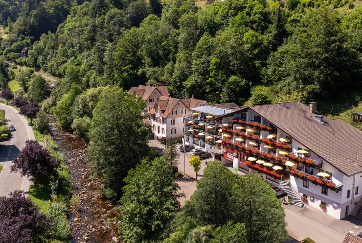 Ringhotel Sonnenhof in Baiersbronn, ein charmantes 4-Sterne-Hotel im Schwarzwald mit bunten Balkon-Sonnenschirmen, umgeben von üppig grünen Waldhügeln. | © Ringhotels Sonnenhof in Baiersbronn