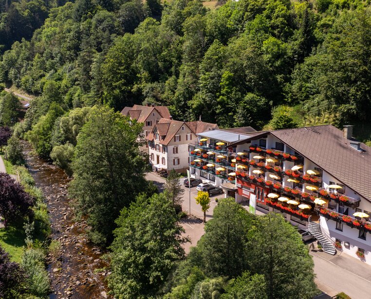 Ringhotel Sonnenhof in Baiersbronn, ein charmantes 4-Sterne-Hotel im Schwarzwald mit bunten Balkon-Sonnenschirmen, umgeben von üppig grünen Waldhügeln. | © Ringhotels Sonnenhof in Baiersbronn