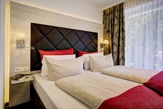 Stilvolles Doppelzimmer mit roten Akzenten, Lederkopfteil und natürlichem Licht im Ringhotel Sonnenhof in Baiersbronn, einem 4-Sterne-Hotel im Schwarzwald | © Ringhotel Sonnenhof in Baiersbronn
